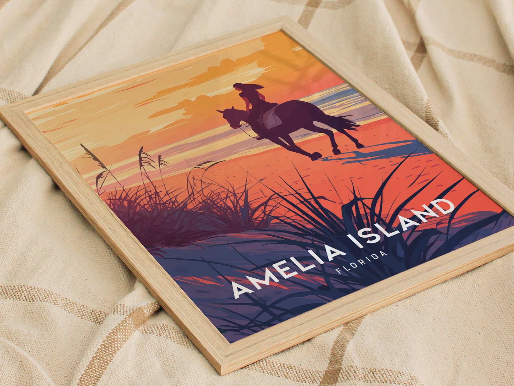 A framed poster depicting a silhouette of a horseback rider on a beach during a vibrant sunset, with the text Amelia Island Florida at the bottom.