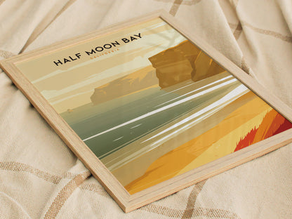 Framed Half Moon Bay poster depicting a serene coastal scene with golden cliffs and shimmering waves, placed on a beige fabric background.