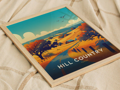 A framed poster titled Hill Country Texas depicts a vibrant landscape with rolling hills, trees, and a winding path under a blue sky, resting on a textured fabric.