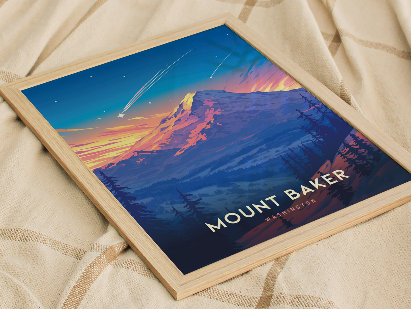 Framed Mount Baker poster featuring a colorful depiction of the mountain, with vibrant sunset hues and a shooting star, resting on a patterned fabric background.