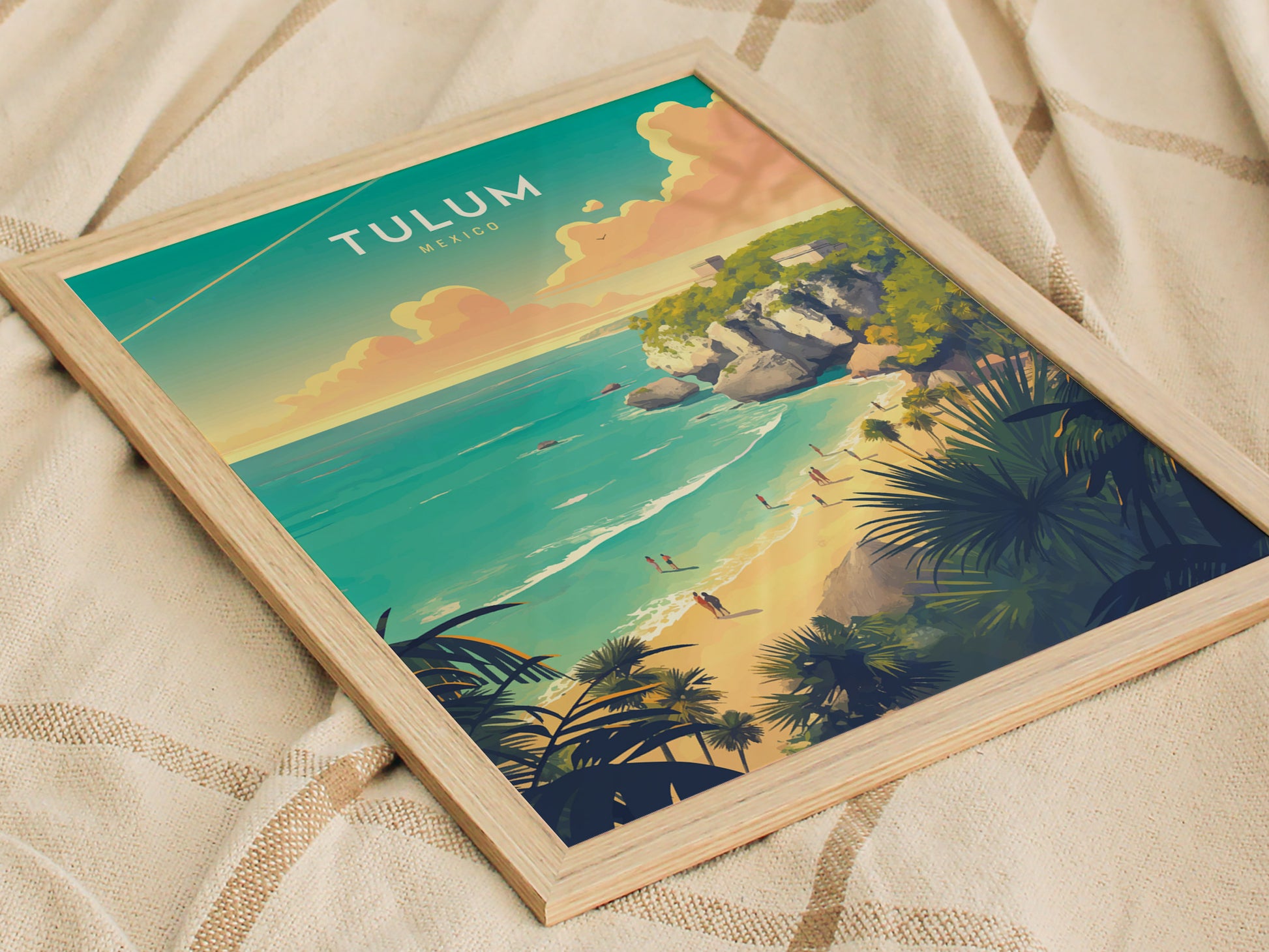 A framed Tulum Mexico poster lies on a textured fabric, showcasing vibrant artwork of a beach with turquoise waters, limestone cliffs, and lush greenery under a colorful sky.