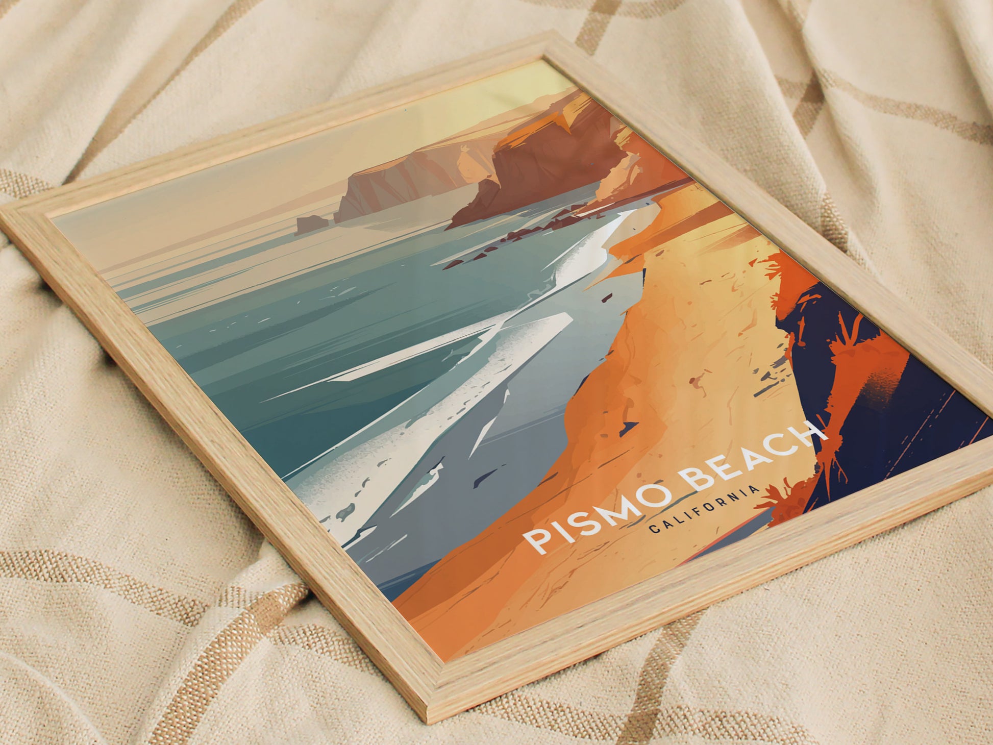 Framed poster featuring an artistic depiction of Pismo Beach, California, showcasing vibrant orange cliffs, a serene ocean, and a sandy shore, placed on a textured fabric background.