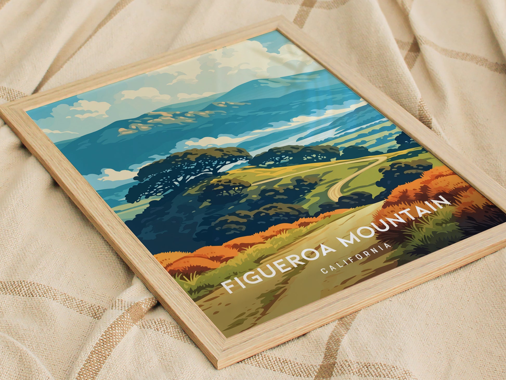A colorful illustration of Figueroa Mountain in California, featuring rolling hills, lush greenery, and a vibrant sky. The poster is framed and resting on a textured beige surface, highlighting the scenic beauty of the landscape.