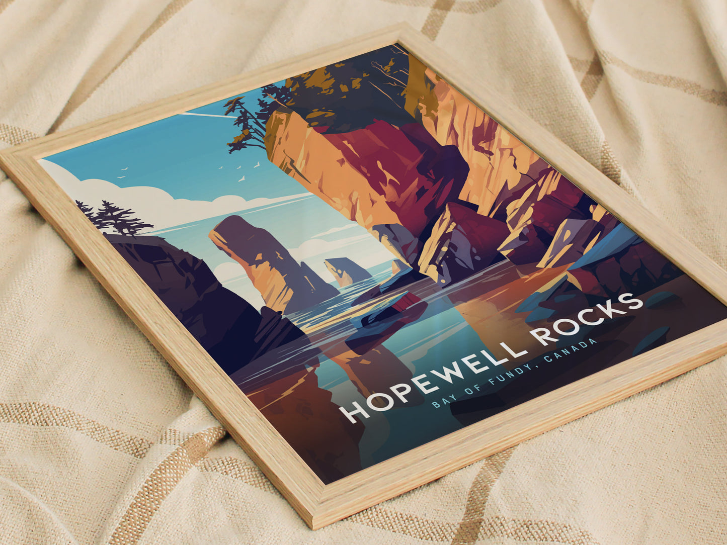 A framed poster of Hopewell Rocks depicts stylized cliffs and ocean scenery in vibrant colors, lying on a beige fabric. Text reads Hopewell Rocks Bay of Fundy, Canada.