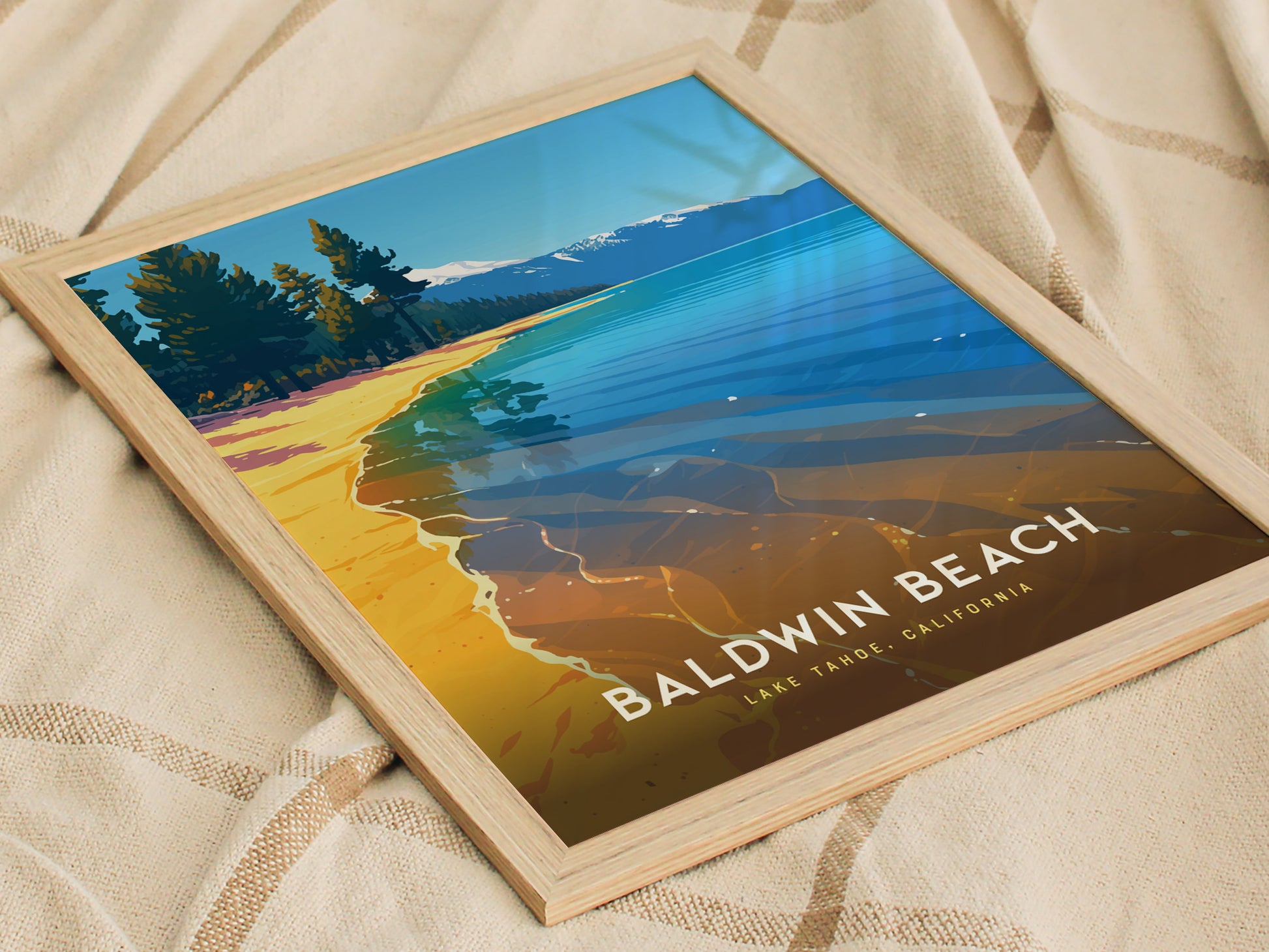 Framed poster of Baldwin Beach, Lake Tahoe, featuring vibrant blue waters, golden sand, and pine trees under a clear sky, placed on a patterned fabric.