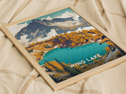 A framed poster of Wing Lake, Washington, featuring vibrant turquoise waters, surrounded by colorful autumn trees and rugged mountain peaks, rests on a beige fabric surface.