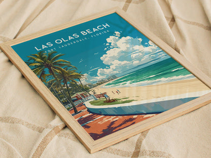 Framed Las Olas Beach poster featuring palm trees, a sandy beach, and ocean waves, resting on a textured fabric. Bright blue sky with clouds adds a tropical feel.