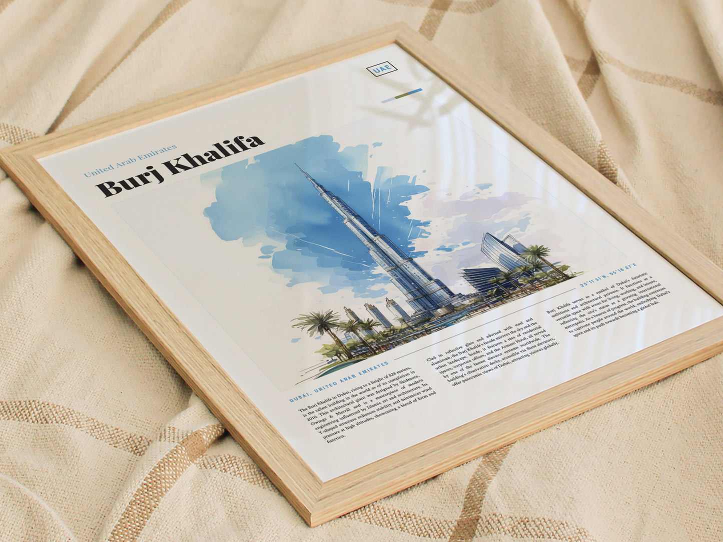 Framed poster of the Burj Khalifa featuring a watercolor illustration, placed on a beige fabric with a subtle pattern. The artwork includes text about the iconic Dubai skyscraper.