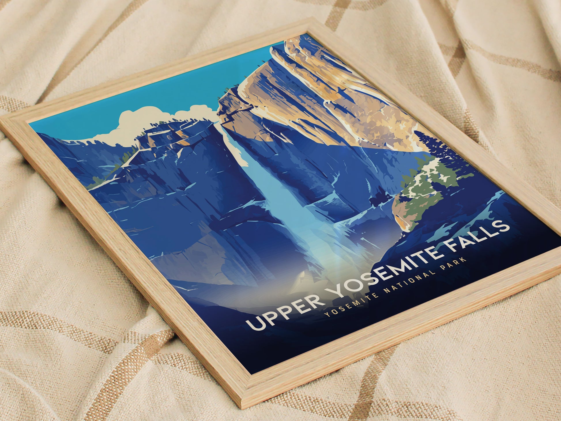 Framed poster of Upper Yosemite Falls on a beige fabric background, featuring a stylized depiction of the waterfall cascading down blue and tan cliffs under a clear sky.
