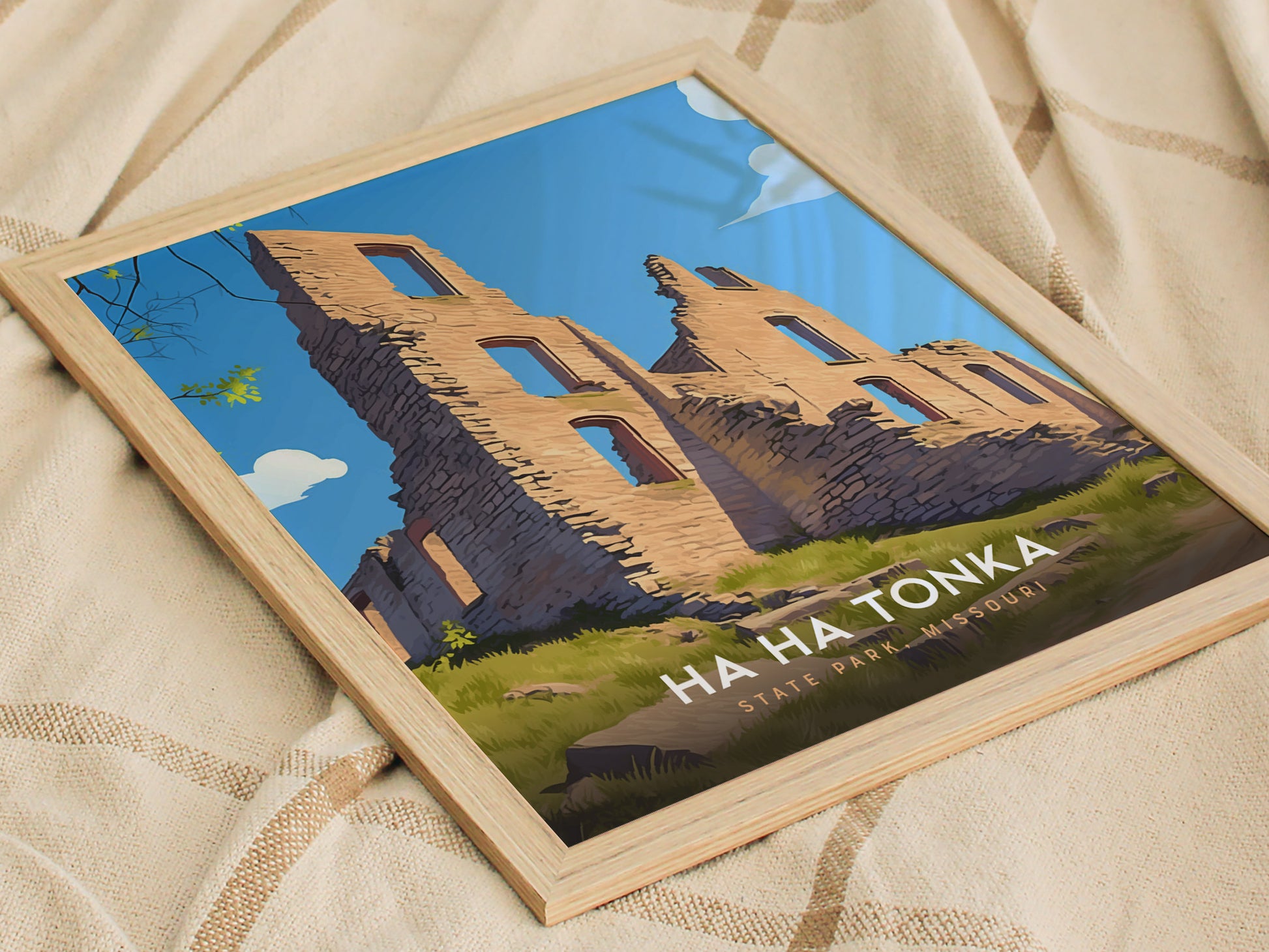 Framed artwork depicting the ruins of Ha Ha Tonka State Park in Missouri, showcasing stone structures against a clear blue sky. The poster rests on a beige, textured fabric.