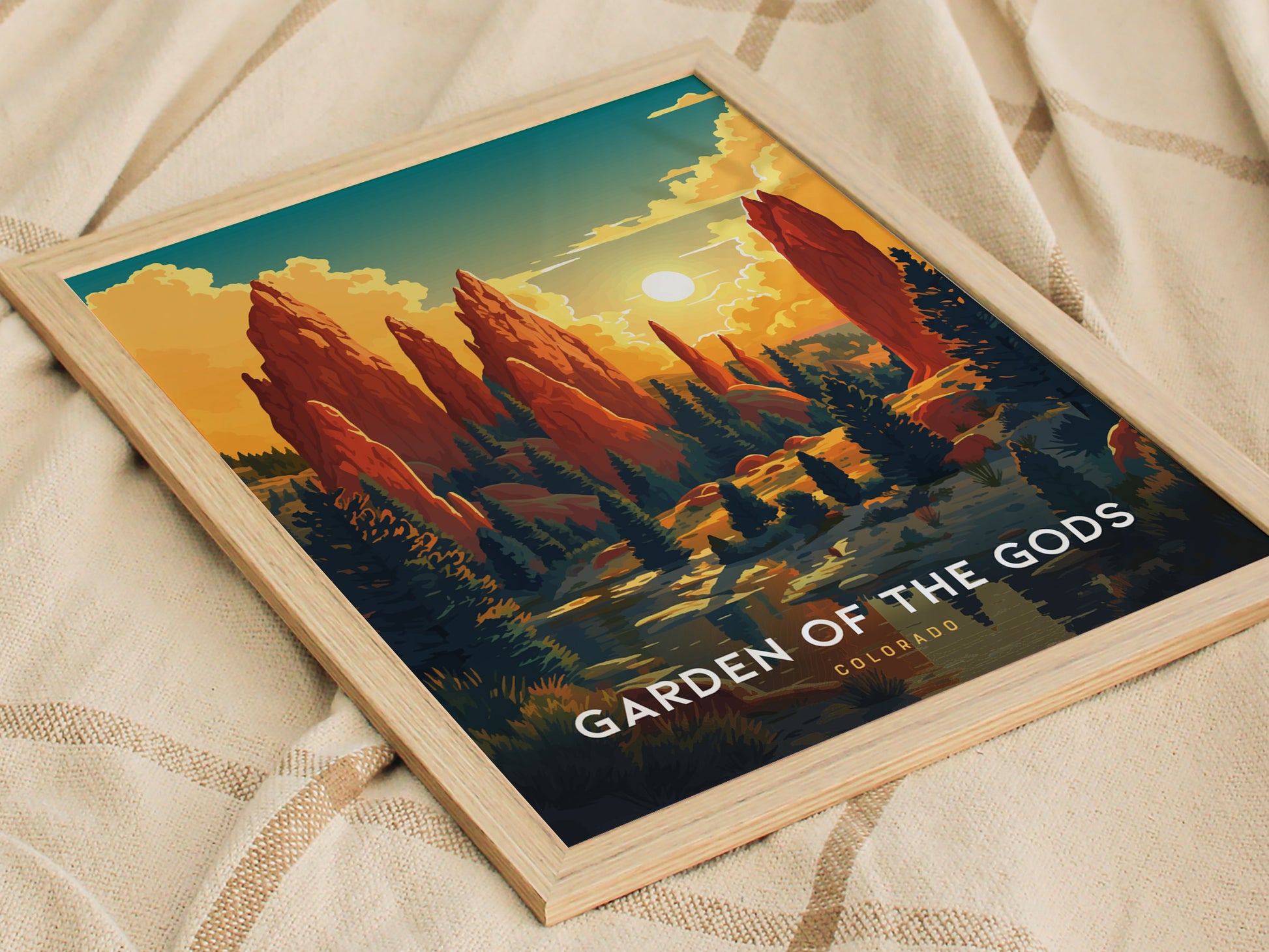 A framed poster of Garden of the Gods features vibrant red rock formations against a sunset sky, placed on a textured beige fabric.