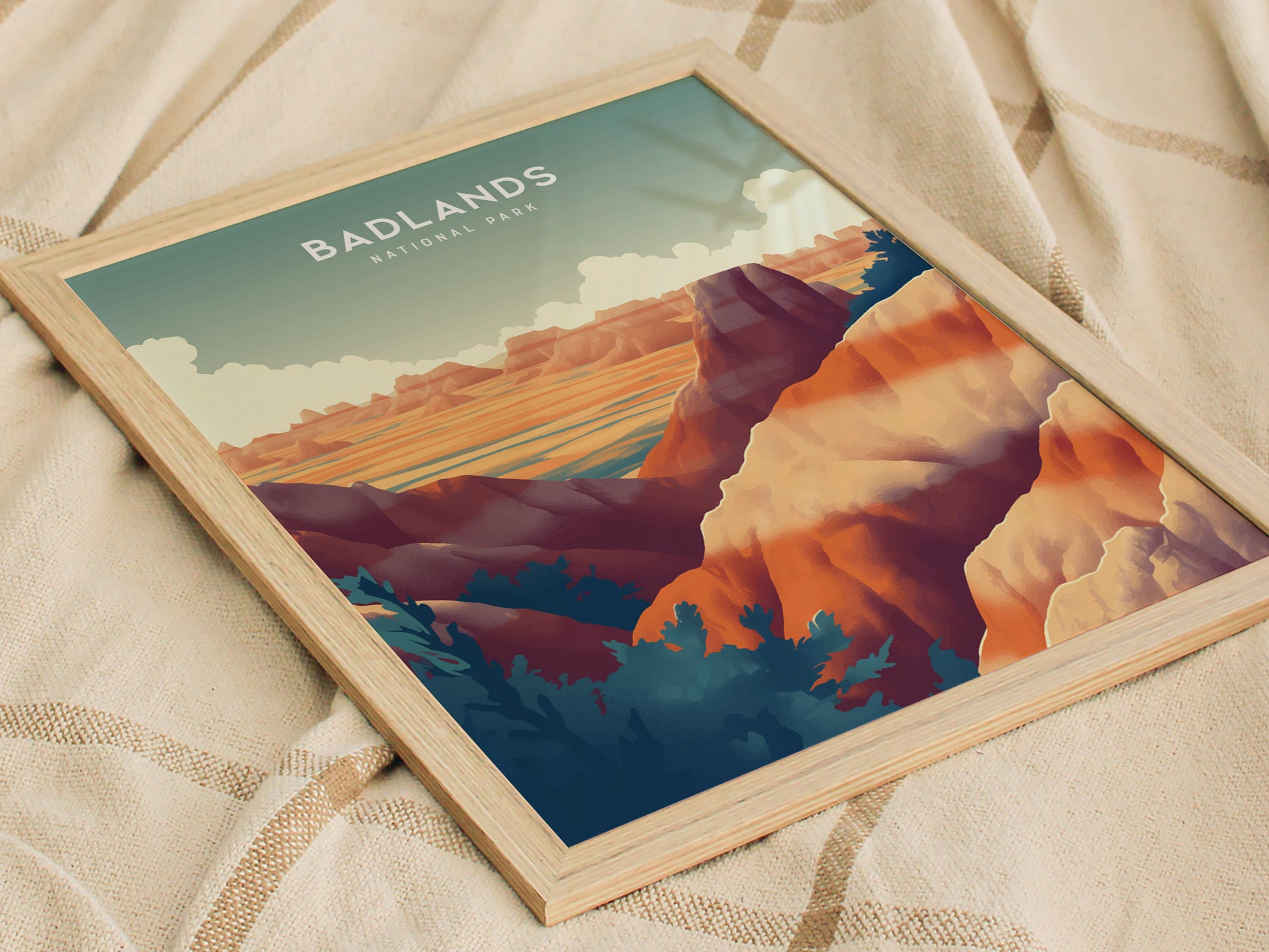 A framed art print of Badlands National Park features vibrant, colorful rock formations and a serene sky, placed on a textured beige fabric.
