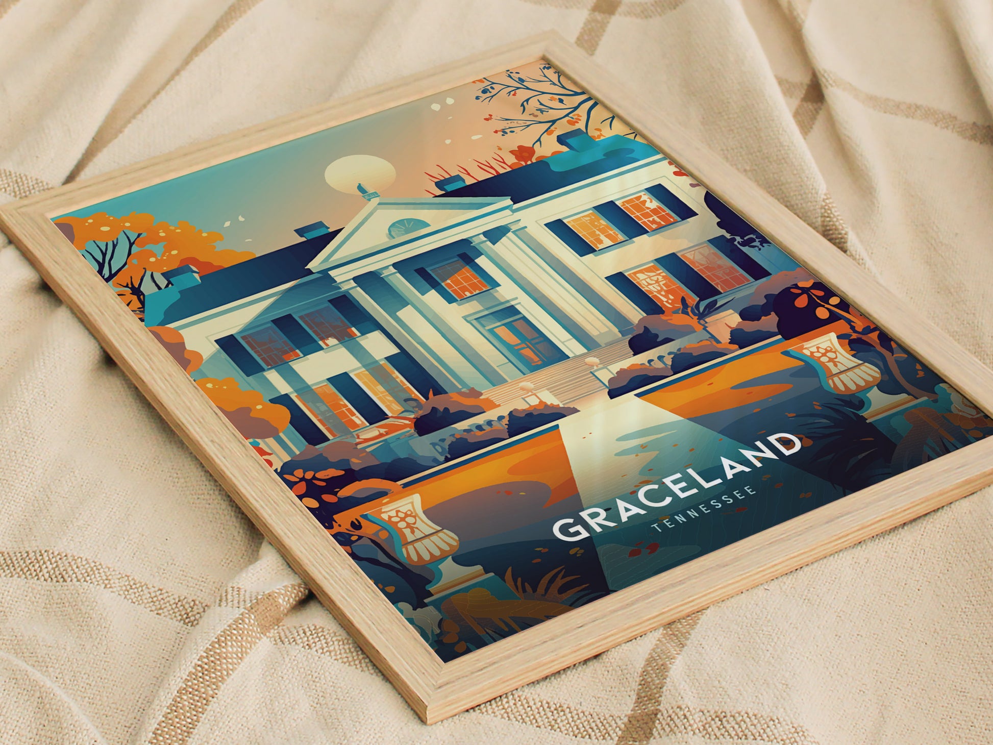 A framed poster depicting the iconic façade of Graceland, surrounded by vibrant autumn foliage, rests on a soft beige fabric. The text Graceland Tennessee is visible at the bottom.