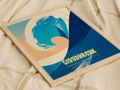 A framed surf poster with abstract blue and beige wave design, titled Cloudbreak Tavarua Island, Fiji, placed on a textured fabric background.