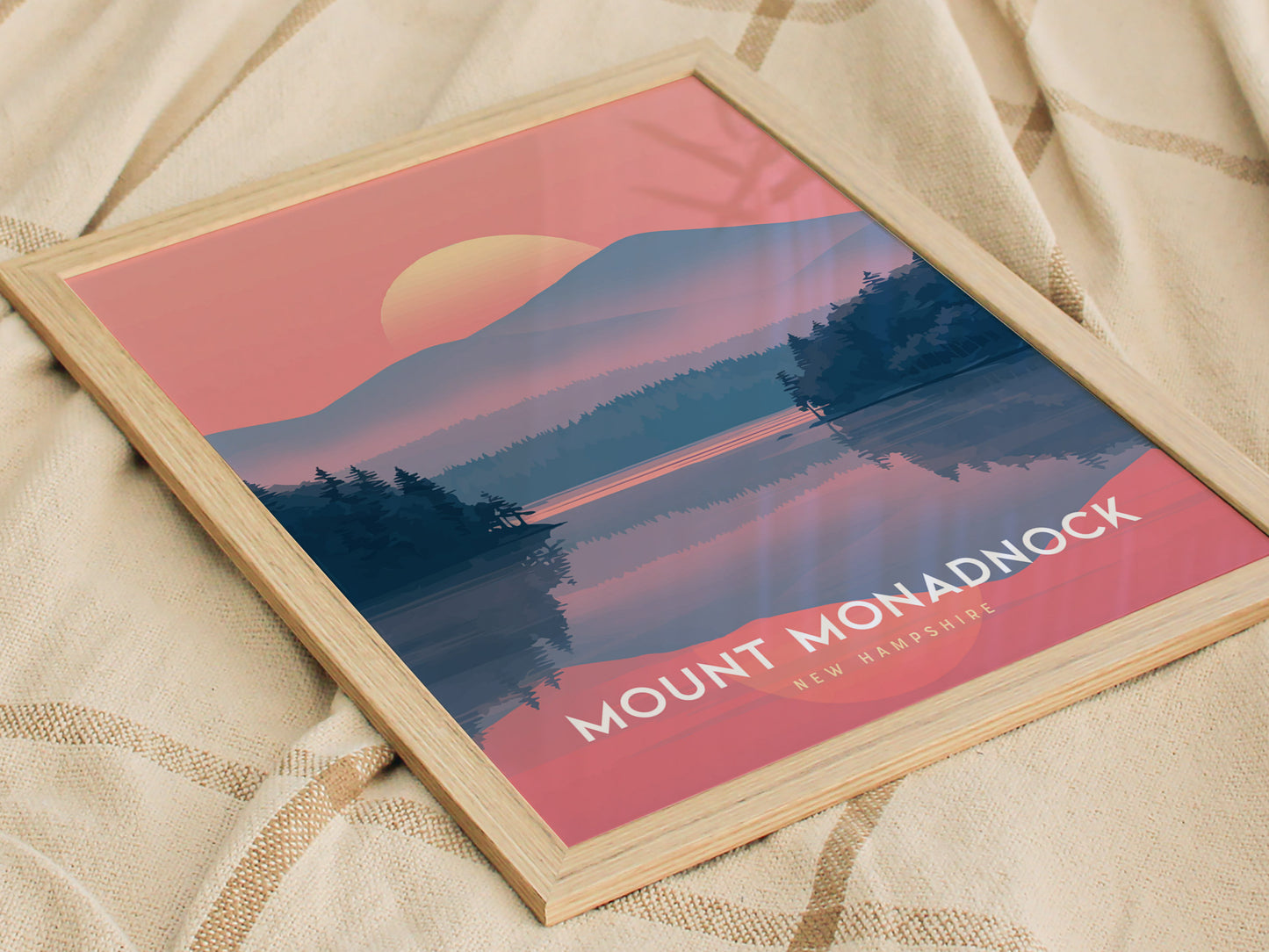 A framed poster of Mount Monadnock, New Hampshire, features a sunset over a forested landscape with a reflective lake, set against a pink and blue gradient sky.