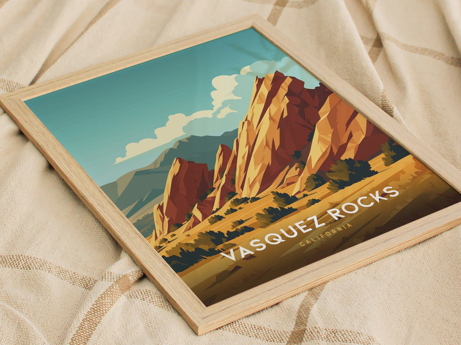 Framed poster of Vasquez Rocks featuring vibrant, stylized sandstone formations under a blue sky, resting on a patterned fabric surface. Text reads Vasquez Rocks, California.