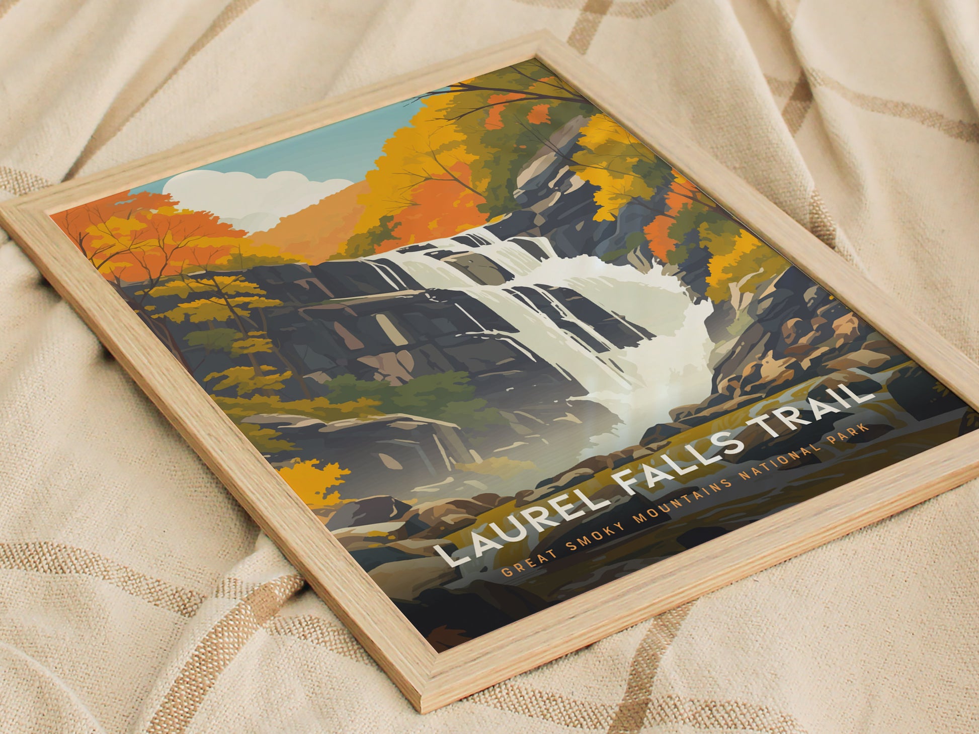 A framed poster of the Laurel Falls Trail features a stylized waterfall surrounded by autumn foliage, set against a soft fabric background. Text reads Great Smoky Mountains National Park.