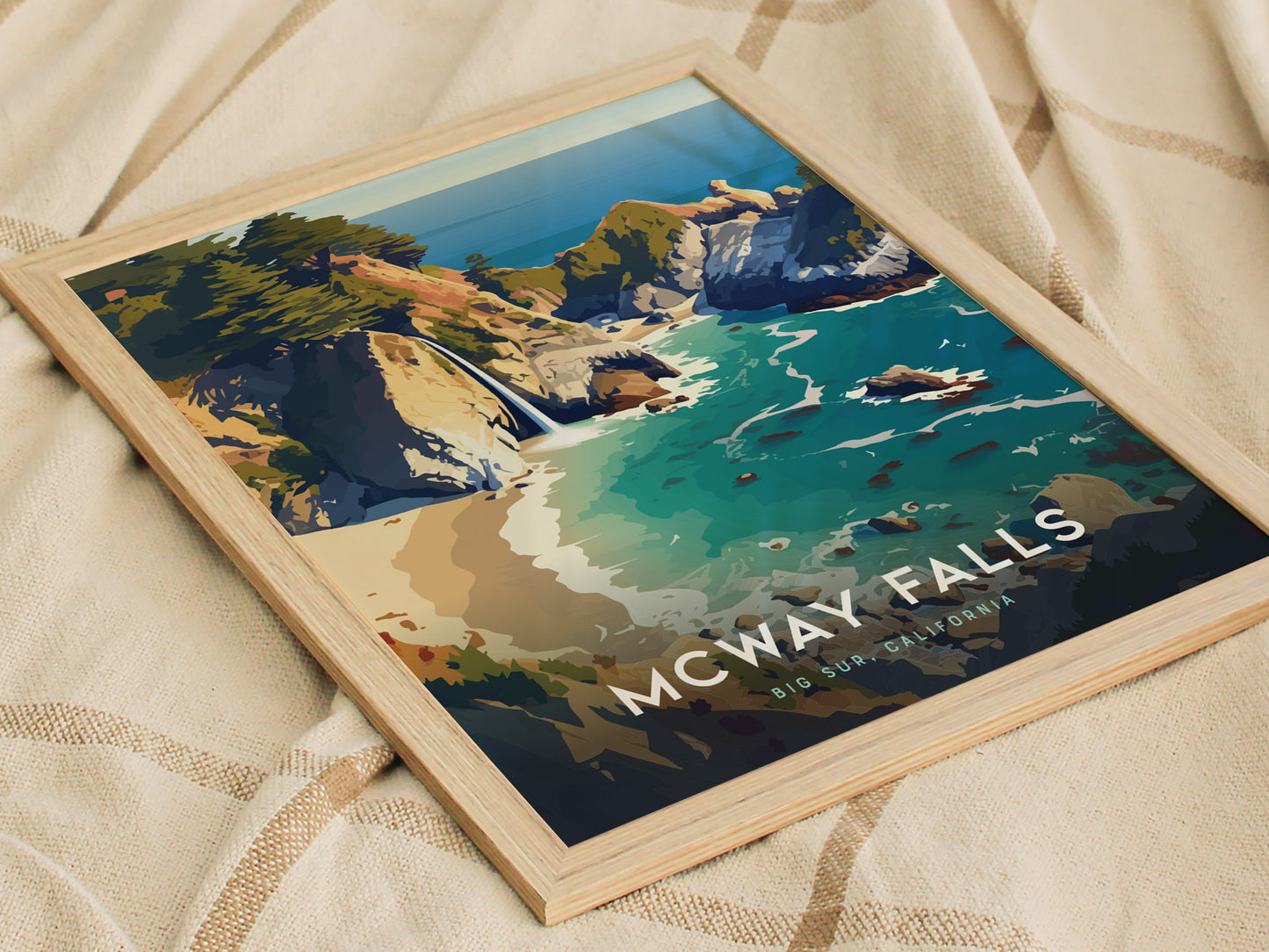 Framed poster of McWay Falls in Big Sur, California, showcasing a stylized illustration of cliffs, turquoise waters, and a waterfall, placed on a beige patterned fabric.