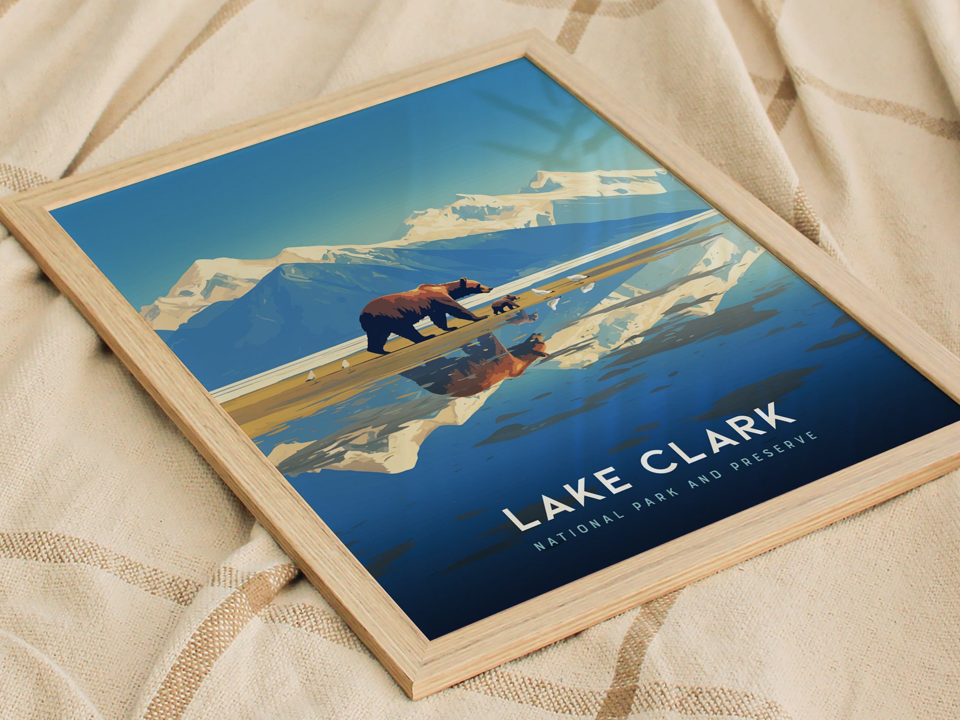 A framed poster of Lake Clark National Park features a bear and cub with a mountainous backdrop, reflecting in a serene lake.