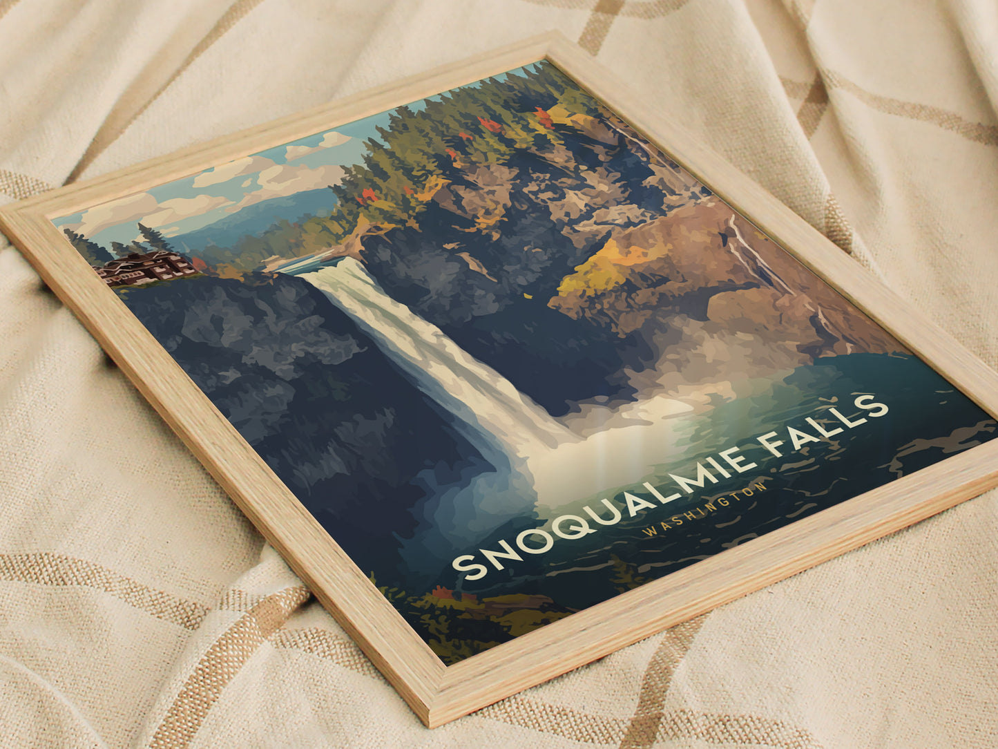 A framed poster of Snoqualmie Falls features a vibrant waterfall scene with lush greenery and dramatic cliffs, set against a soft fabric background. The text reads Snoqualmie Falls, Washington.