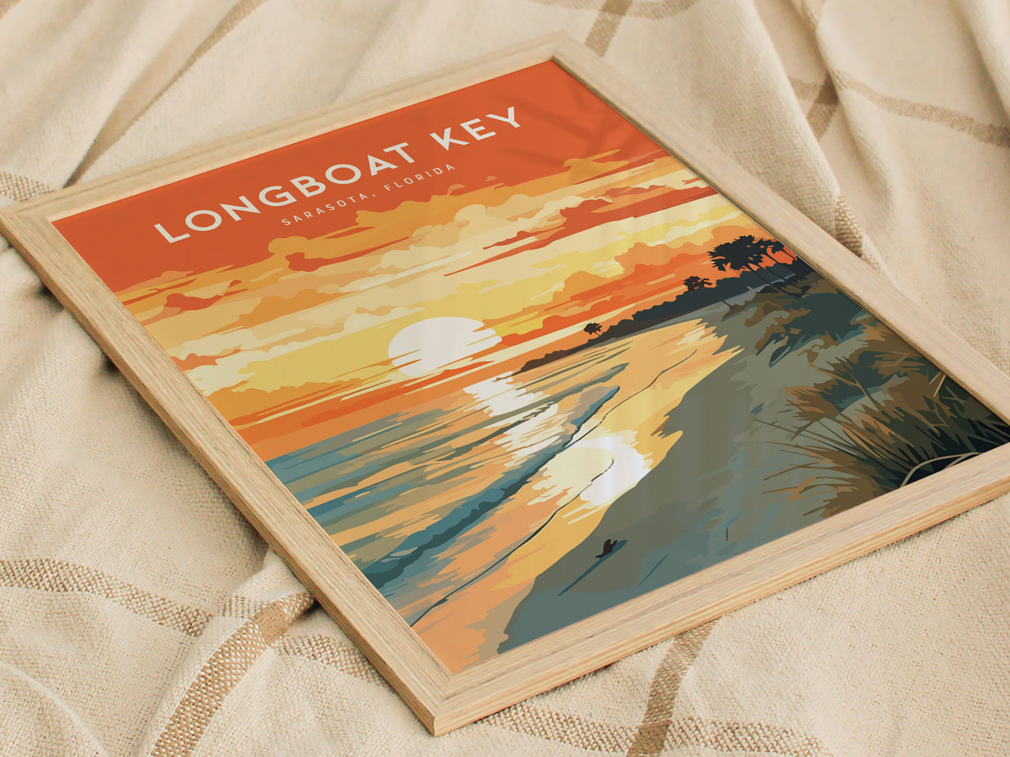 The image shows a framed poster of Longboat Key, Sarasota, Florida, with a sunset scene featuring vibrant orange and yellow hues, a reflective ocean, and silhouettes of palm trees. The poster rests on a textured beige fabric.