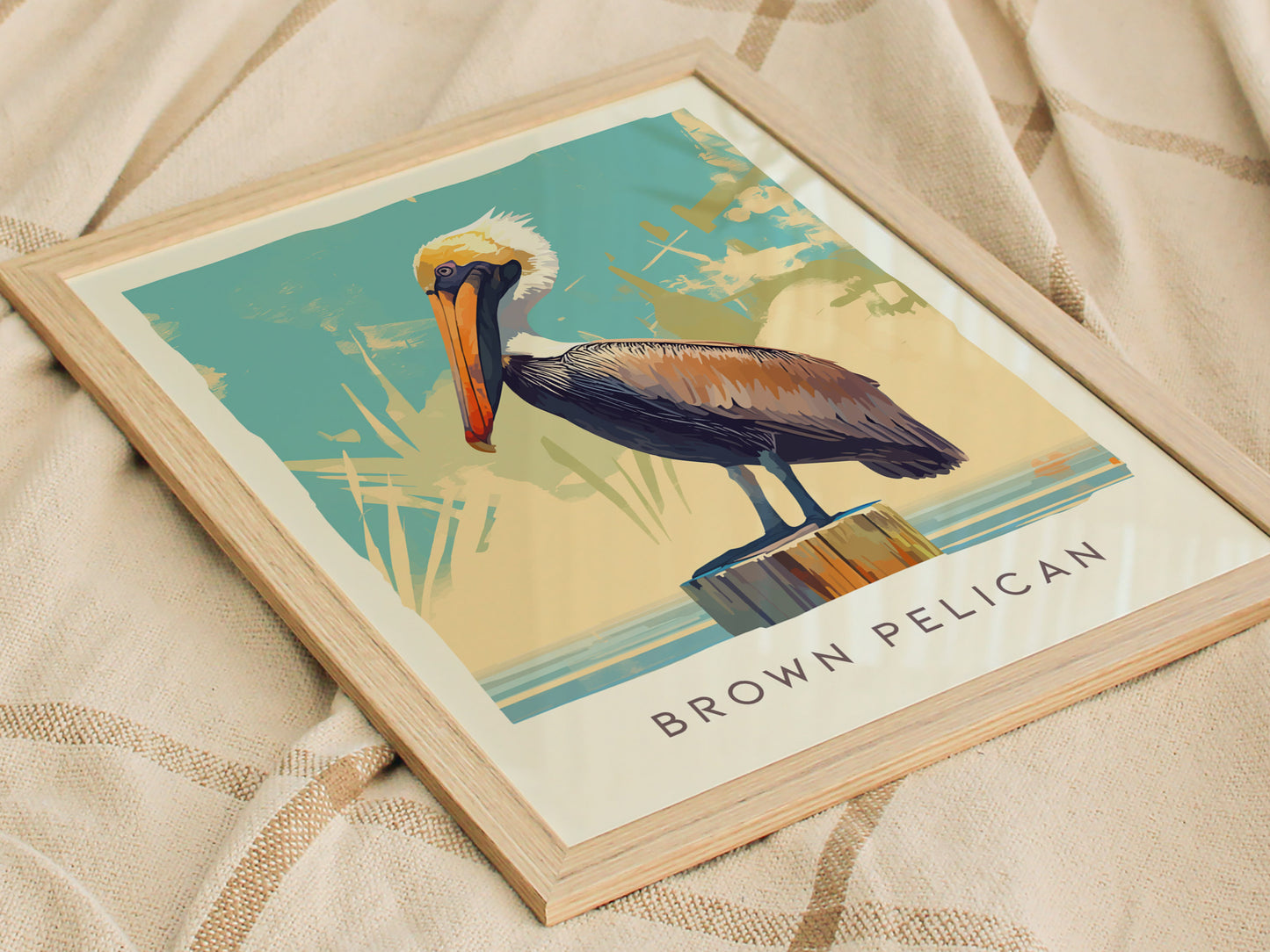 A framed poster featuring an illustrated brown pelican perched on a post against a stylized background. The artwork is set on a soft, textured fabric surface.