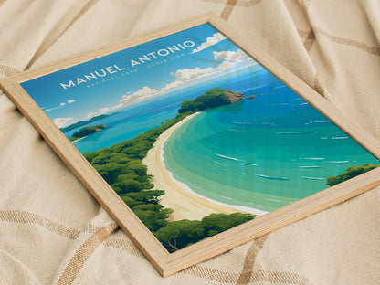 A framed poster of Manuel Antonio National Park rests on a fabric surface, depicting a vibrant coastal scene with turquoise waters, white sandy beaches, and lush green foliage.