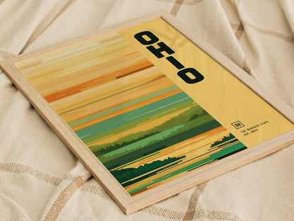 A framed poster featuring the word OHIO in bold letters on a minimalist design with horizontal stripes in earthy tones, resting on a textured fabric surface.