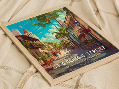 A vibrant poster depicting St. George Street in St. Augustine, Florida, with colorful buildings, lush greenery, and a clear blue sky, framed and placed on a textured fabric background.