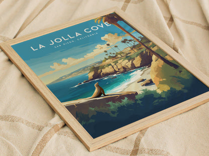 Framed La Jolla Cove poster featuring a stylized coastal scene with sea cliffs, palm trees, and ocean waves, resting on a textured beige fabric background.