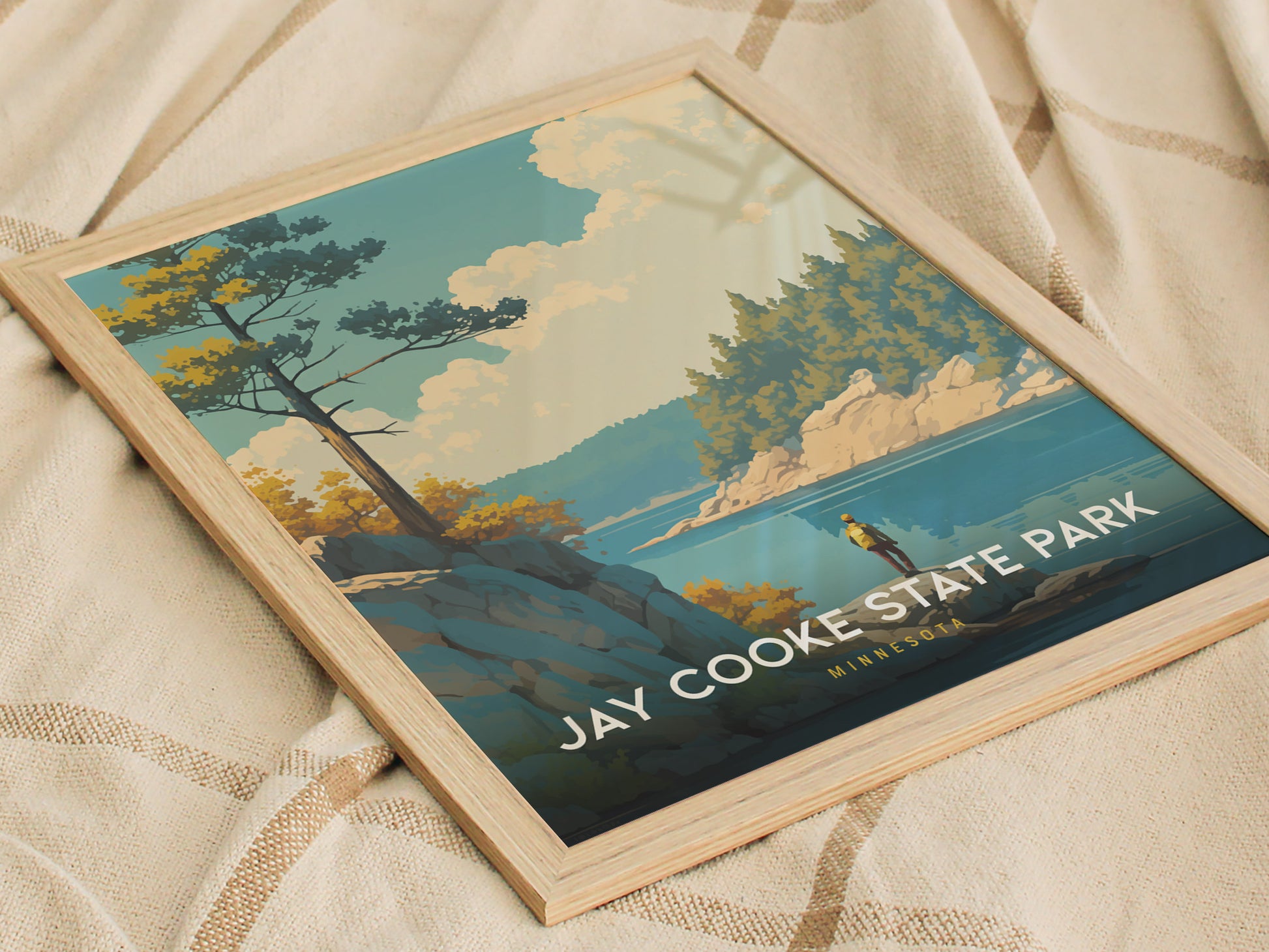 Framed Jay Cooke State Park poster resting on a patterned fabric, featuring a scenic landscape with trees, rocks, and a river under a blue sky.