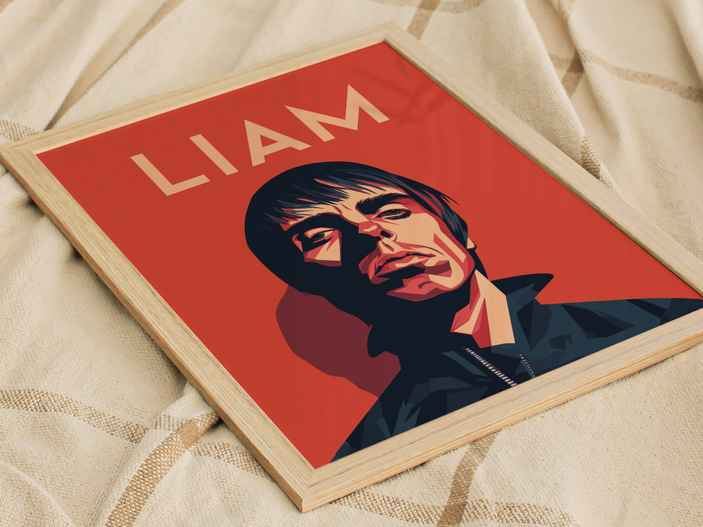 A framed poster with a stylized portrait of a man on a red background, featuring the name Liam at the top, placed on a textured fabric surface.