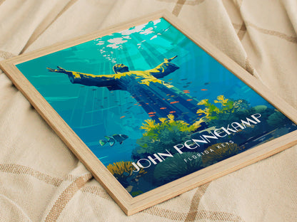 Framed poster depicting an underwater statue with outstretched arms, surrounded by coral and fish, titled John Pennekamp Florida Keys, resting on a textured fabric surface.