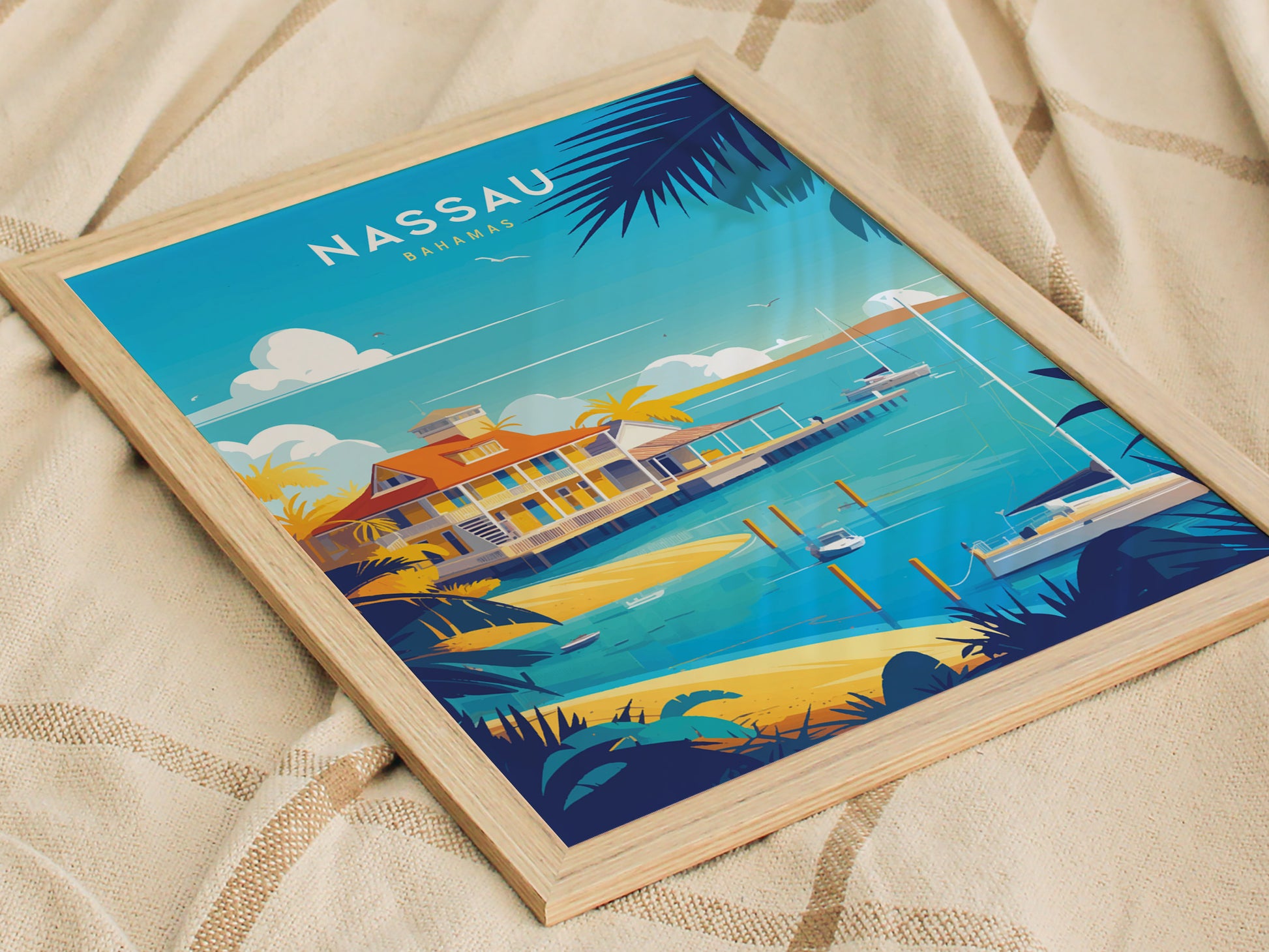 A framed poster depicting a vibrant Nassau, Bahamas scene with a beach house, turquoise water, and sailboats, set against a bright blue sky, resting on a beige fabric.