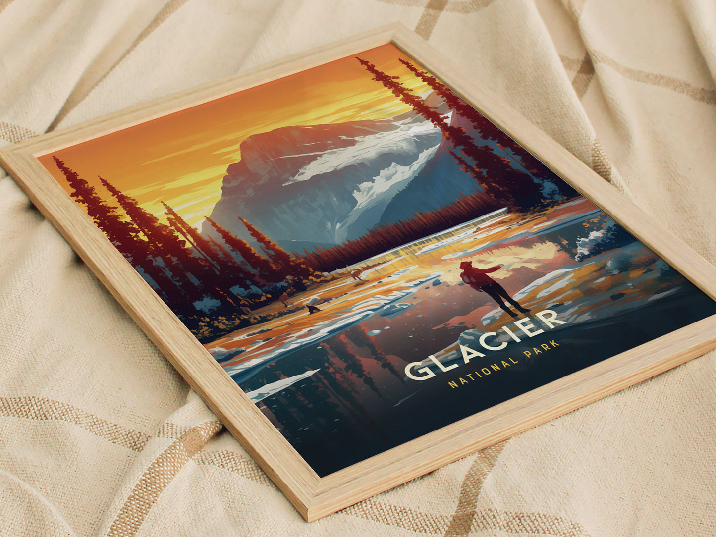 A framed poster of Glacier National Park features a vibrant illustration of mountains, pine trees, and a person standing by a reflective lake at sunset.