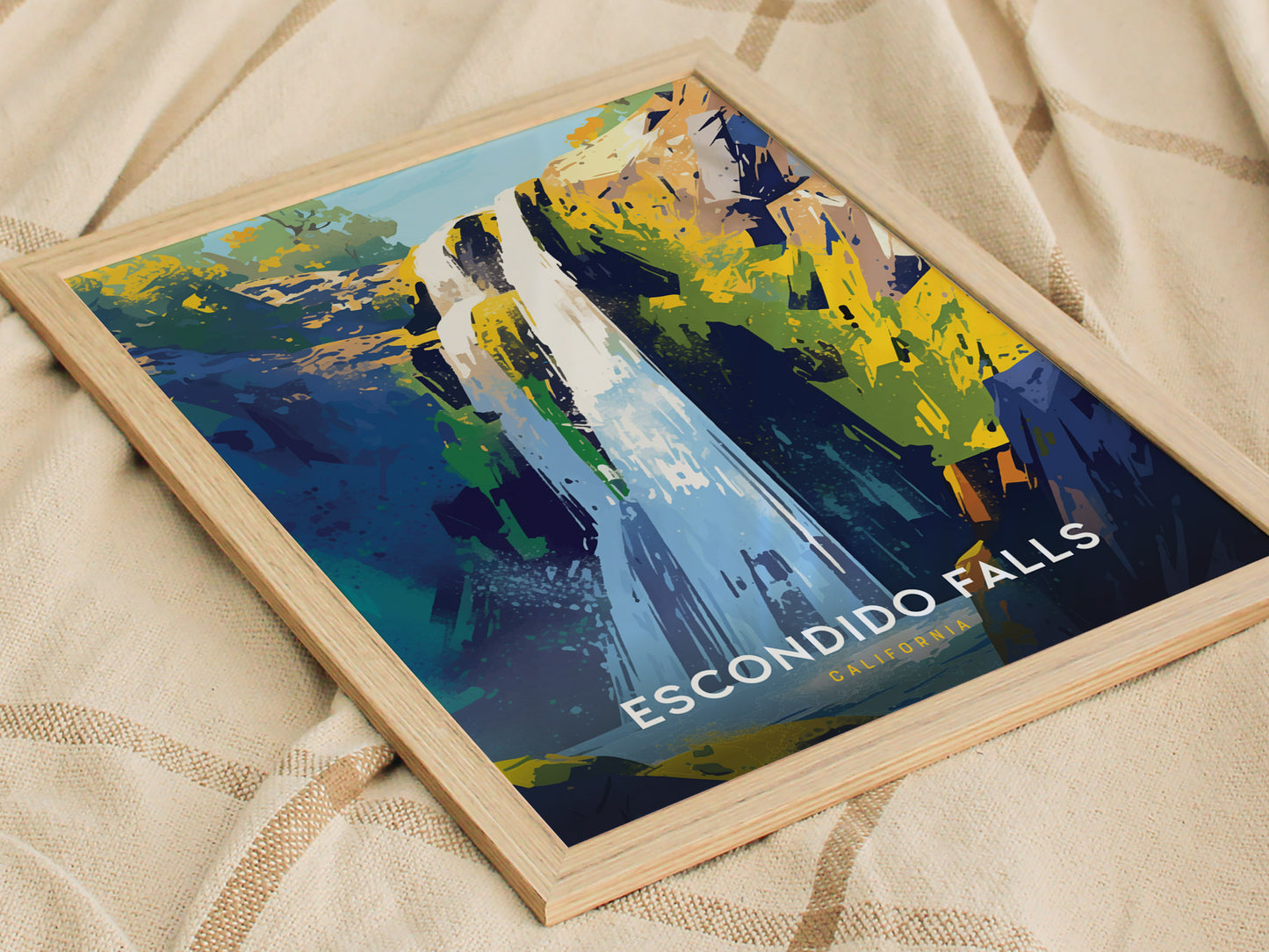 A framed art print of Escondido Falls features a stylized depiction of a waterfall with vibrant blues, greens, and yellows. Its placed on a textured beige fabric.