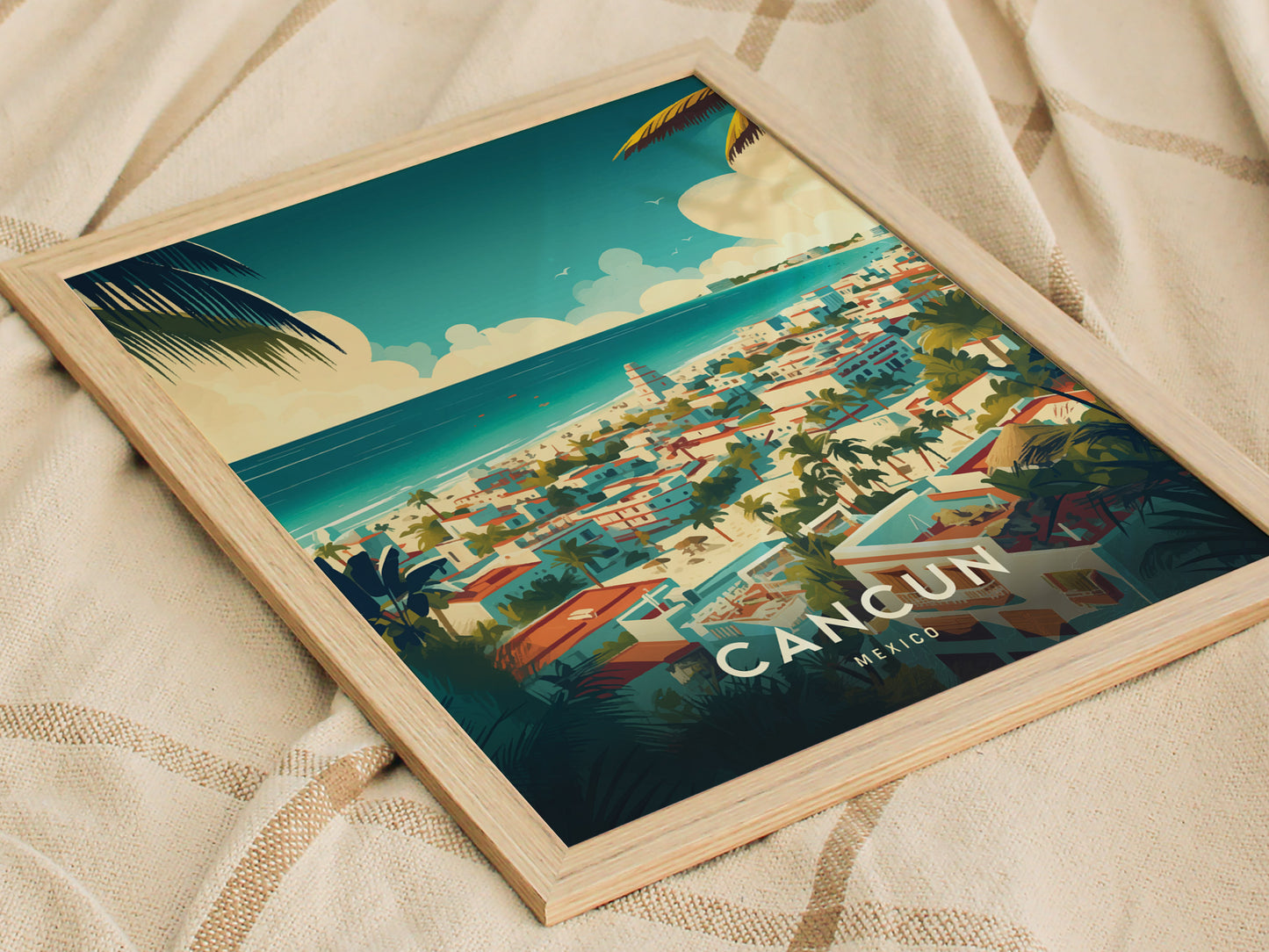 A framed poster of Cancun, Mexico, featuring a colorful illustration of a coastal town with palm trees and turquoise waters, rests on a beige fabric surface.