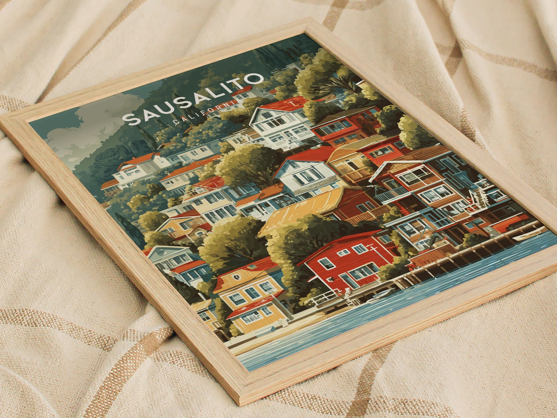 A framed artwork features a vibrant illustration of Sausalito, showcasing colorful houses nestled on a hillside near the water. The scene captures a picturesque coastal vibe with lush greenery and a serene atmosphere.