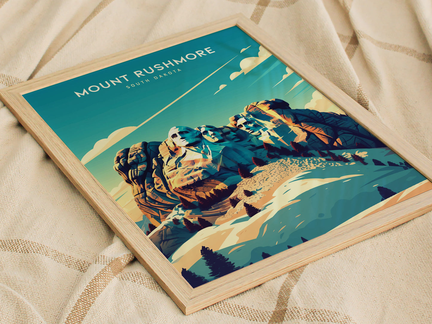 A framed Mount Rushmore poster featuring a colorful illustration of the monument against a vibrant sky, resting on a textured beige fabric surface.