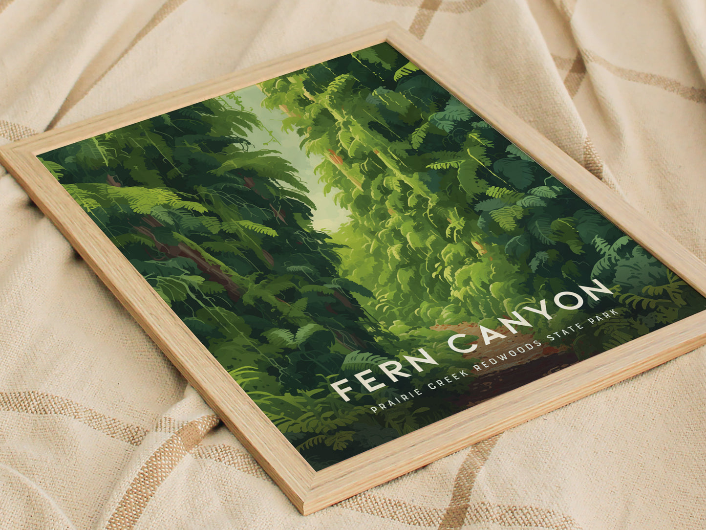 Framed poster featuring lush green ferns and a path through Fern Canyon, Prairie Creek Redwoods State Park, resting on a beige fabric with a checkered pattern.