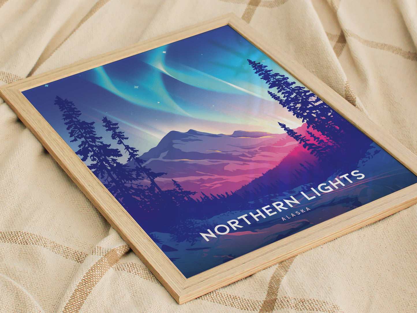 Framed artwork depicting the Northern Lights with vibrant green and violet hues over a mountain landscape and silhouetted trees, placed on a textured fabric surface.