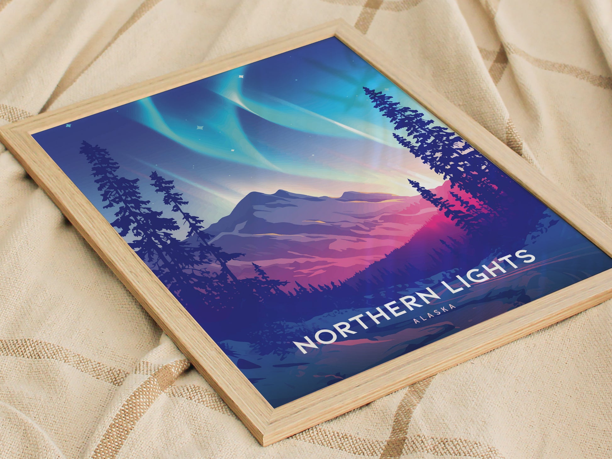 Framed artwork depicting the Northern Lights with vibrant green and violet hues over a mountain landscape and silhouetted trees, placed on a textured fabric surface.