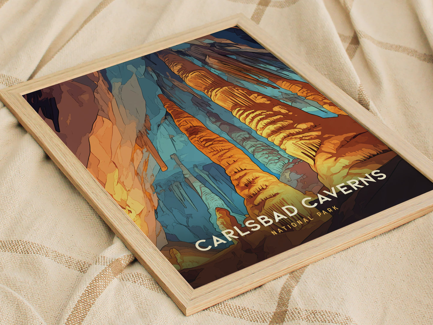 A framed poster of Carlsbad Caverns National Park displays vibrant rock formations in orange, blue, and brown hues, resting on a soft, beige fabric surface.
