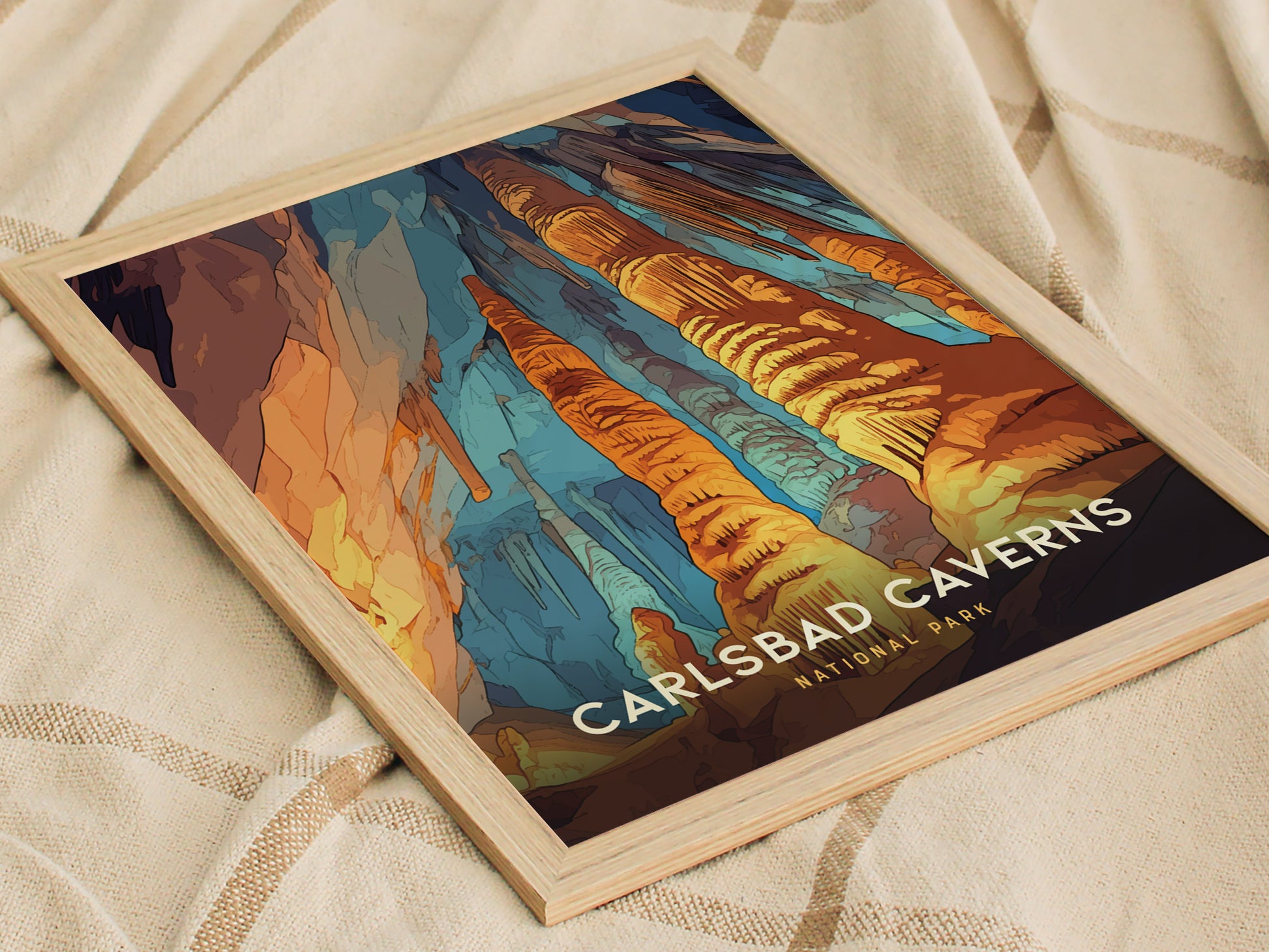 A framed poster of Carlsbad Caverns National Park displays vibrant rock formations in orange, blue, and brown hues, resting on a soft, beige fabric surface.