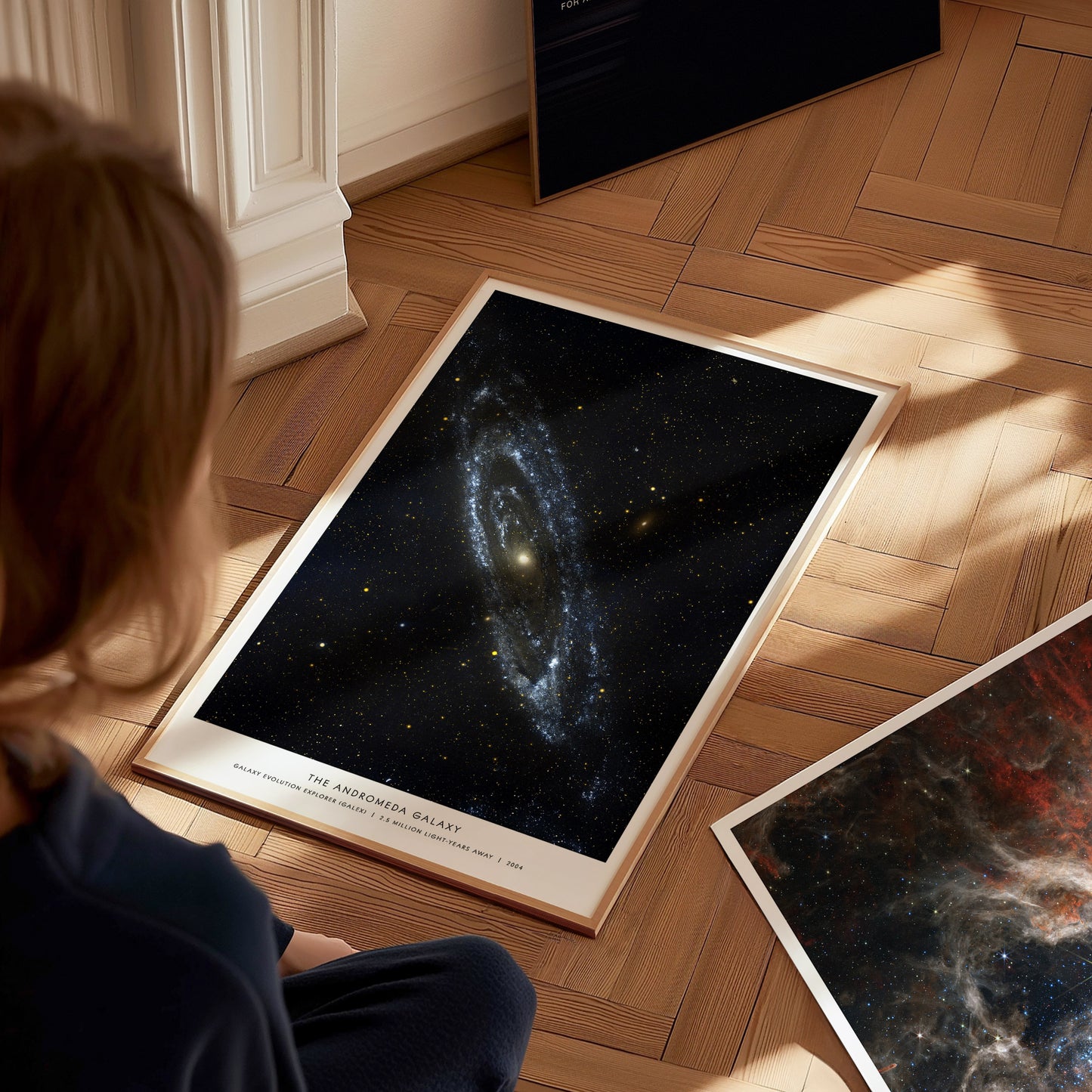 Person sitting on a wooden floor looking at space posters of galaxies