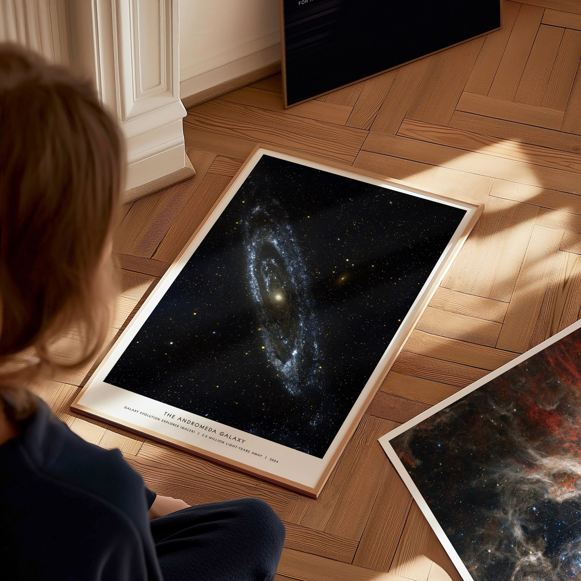 Person sitting on a wooden floor looking at space posters of galaxies