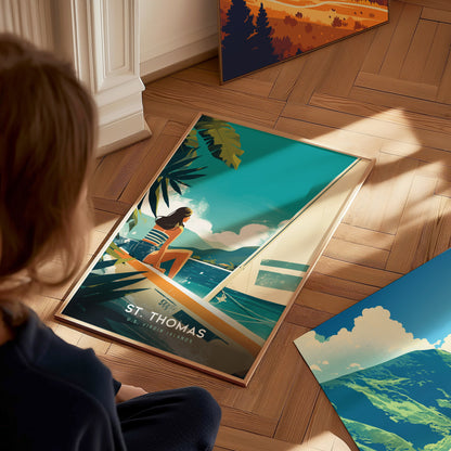 A person sits on a wooden floor admiring a framed St. Thomas U.S. Virgin Islands poster, depicting a woman on a sailboat with tropical greenery and turquoise waters.