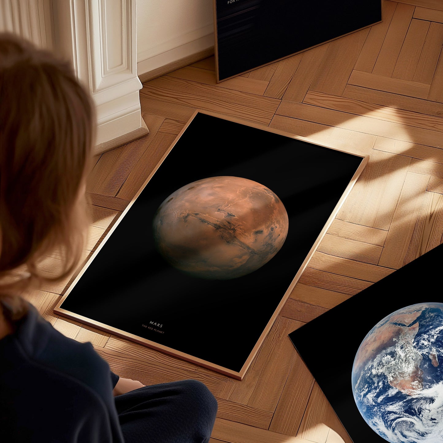 Person looking at a poster of Mars on a wooden floor with another poster of Earth nearby.