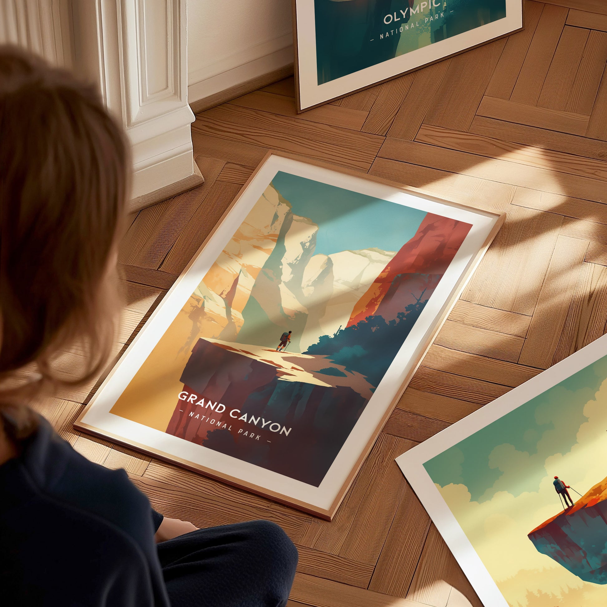 A person sits on a wooden floor, observing framed minimalist wall art of the Grand Canyon. The artwork features vibrant colors and a scenic landscape, capturing the canyons grandeur.