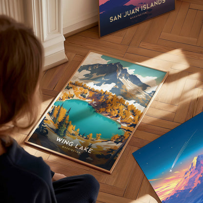 A person observes a framed Wing Lake Washington poster on a wooden floor, depicting vibrant turquoise waters and autumn foliage in a mountainous landscape.